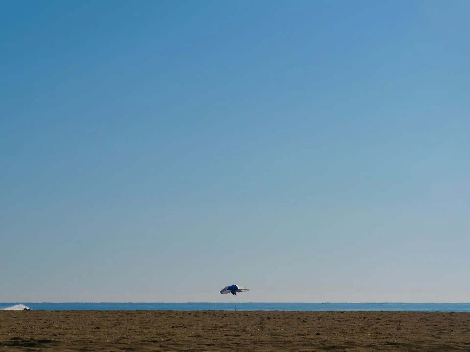 Ombrellone solitario su una spiaggia vuota, immagine della sospensione estiva delle sedute di psicoterapia